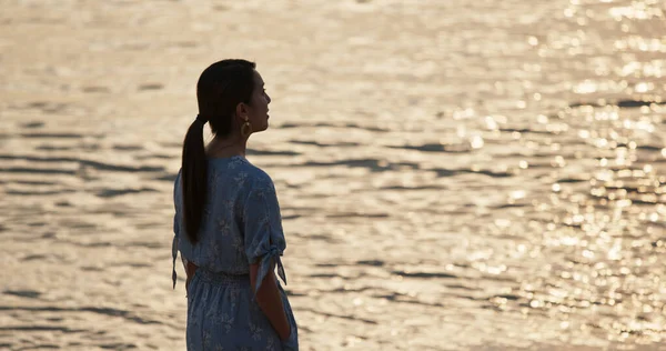 Donna in piedi sulla spiaggia e godere della vista sul mare al tramonto — Foto Stock