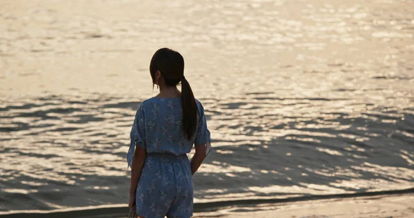 Donna in piedi sulla spiaggia e godere della vista sul mare al tramonto — Foto Stock