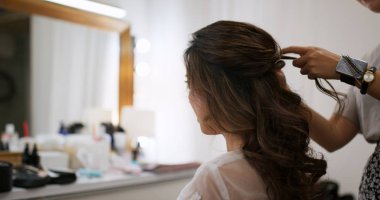 Hairdresser making hairstyle on bride in beauty salon