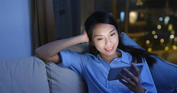 Woman watch at cellphone and sit on sofa in the evening