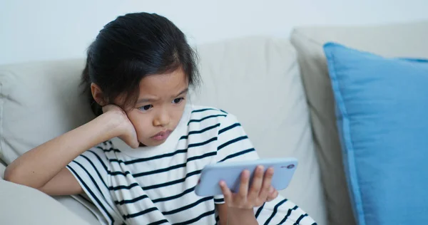 Маленькая девочка смотреть по сотовому телефону дома — стоковое фото
