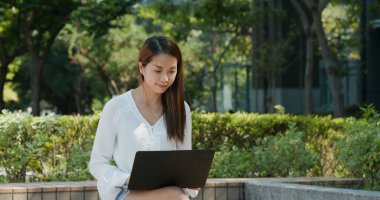 Kadın parkta dizüstü bilgisayarda çalışıyor.