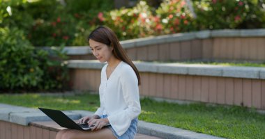 Kadın parkta dizüstü bilgisayarda çalışıyor.