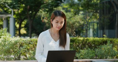 Kadın parkta dizüstü bilgisayarda çalışıyor.