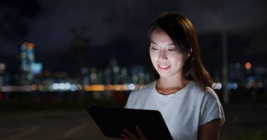 Sokakta akşam vakti tablet bilgisayarda okuyan bir kadın