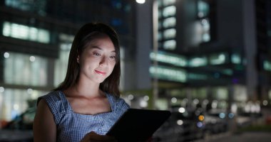İş kadını geceleri dışarıda tablet bilgisayardan kitap okuyor.