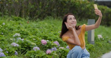 Çiçek tarlasında cep telefonuyla selfie çeken kadın.