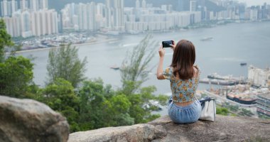 Kadın taşın üzerine oturur ve şehirde akıllı telefon kullanır.