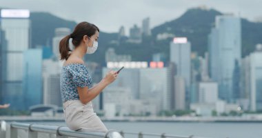 Hong Kong 'da kadın yüz maskesi takıyor ve cep telefonu kullanıyor.