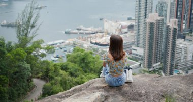 Kadın tepenin zirvesinde oturur ve şehir manzarasının tadını çıkarır.