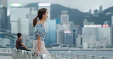 Kadın yüz maskesi takıyor ve Hong Kong 'daki şehre bakıyor.