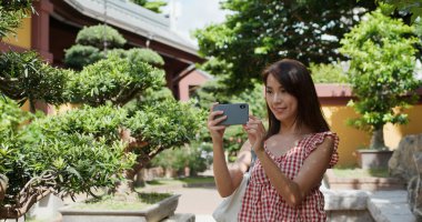 Kadın, Çin bahçesinde fotoğraf çekmek için cep telefonu kullanıyor.