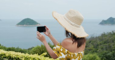 Kadın dağda cep telefonuyla fotoğraf çekiyor.