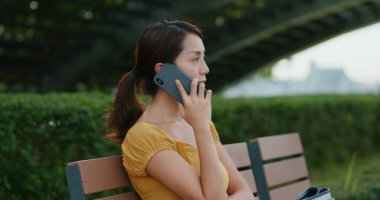 Kadın parkta cep telefonuyla konuşuyor.