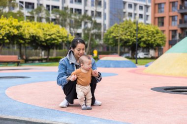 Mom teaching baby walking in sunny park