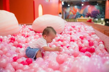 Infant playing happily with balls in pink pit