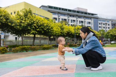 Mother help baby boy walk in park