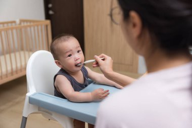 Woman use spoon to feed her baby son
