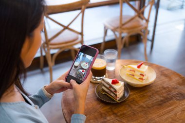 Woman taking photo of cake using mobile phone indoors