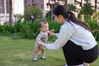 Mother holding baby hand teaching him to walk outdoors