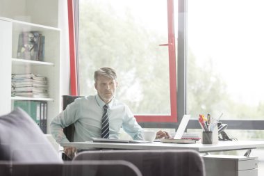 Office penceresinde tarafından masada oturan ciddi iş adamı