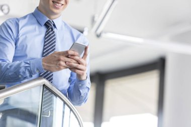 Midsection ofiste dururken smartphone kullanarak gülümseyen iş adamı
