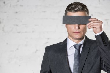 Olgun işadamı ofiste beyaz tuğla duvara karşı kağıt ile gözleri kaplayan
