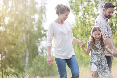 Gülümseyen kız alan üzerinde ağaçlara karşı ebeveynler ile yürüyüş