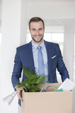 Yeni ofiste karton kutu ile ayakta gülümseyen genç işadamı portresi