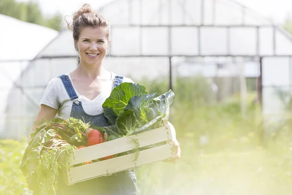 Portrait of smiling woman holding vegetables in crate at farm