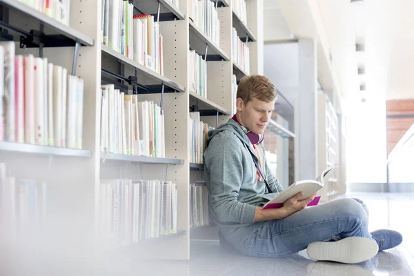 Studentin Liest Buch Gegen Regal Während Sie Universitätsbibliothek Sitzt — Stockfoto