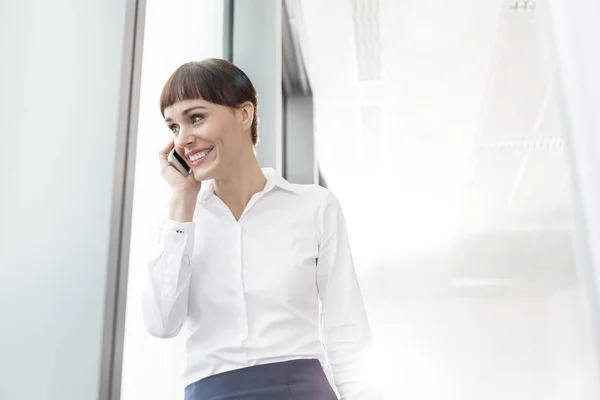 Lächelnde Geschäftsfrau Spricht Smartphone Während Sie Büro Fenster Steht — Stockfoto