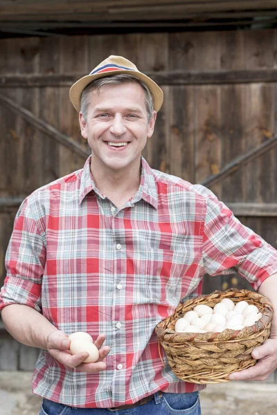 在农场的柳条篮子里抱着鸡蛋的微笑的成熟农民的肖像 — 图库照片