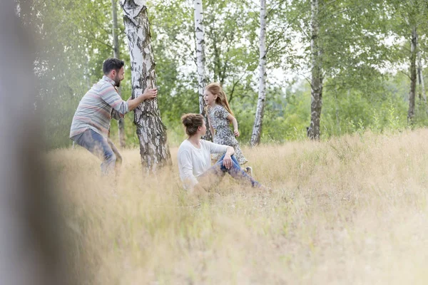 Frau Sitzt Während Mann Mit Tochter Auf Feld Zwischen Bäumen — Stockfoto