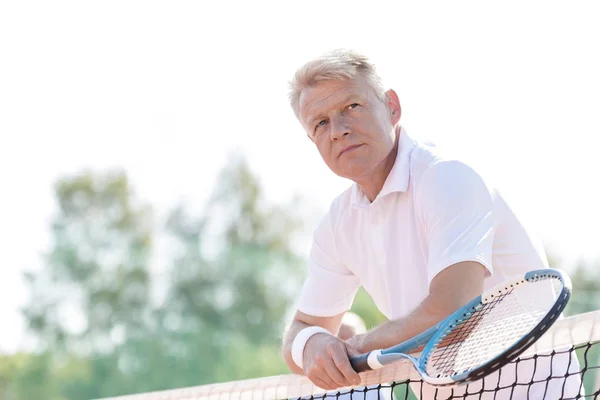 明確な空を背景にもたれながらテニス ラケットを持って思いやりのある中年の男性 — ストック写真