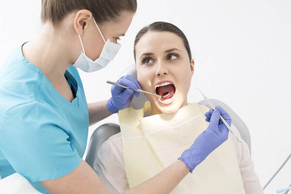 Dentist examining patient mouth with angled mirror and scaler at dental clinic