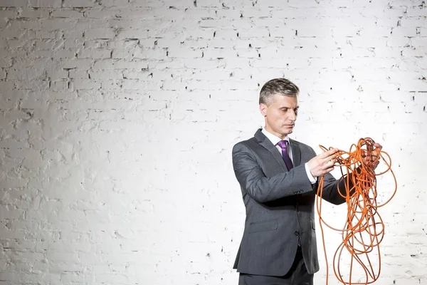 Zelfverzekerde Volwassen Zakenman Houdt Verwarde Rode Kabel Tegen Witte Bakstenen — Stockfoto