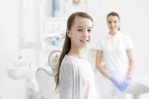 Portrait of smiling girl patient against dentist at clinic