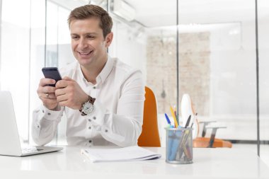 Ofiste Smartphone kullanırken gülümseyen iş adamı