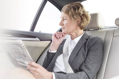Thoughtful businesswoman with newspaper sitting in car clipart
