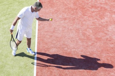 Emin olgun adamın tenis kortunda maç sırasında güneşli günde hizmet yüksek açılı görünüş