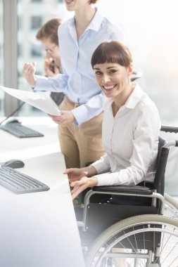 Modern ofiste meslektaşları tarafından çalışan gülümseyen engelli iş kadını portresi
