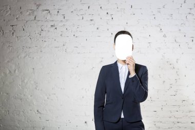 Ofiste beyaz tuğla duvara karşı boş kağıt ile yüz kapsayan genç iş kadını