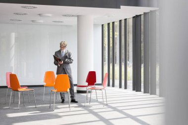 Olgun işadamı yeni ofiste sandalyelerin ortasında dururken belge okuyor