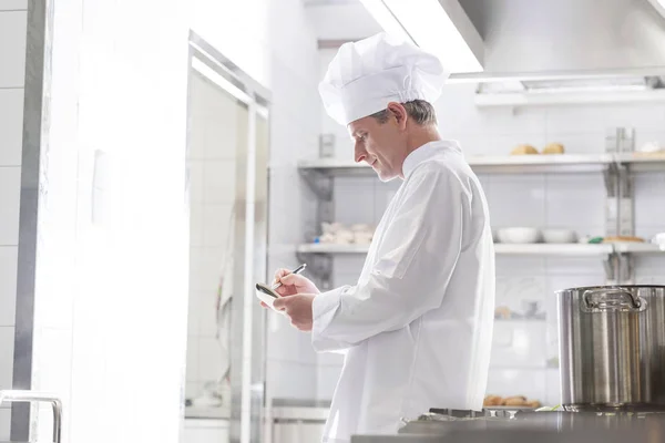 Zijaanzicht Van Chef Kok Schrijven Kladblok Terwijl Keuken Bij Restaurant — Stockfoto