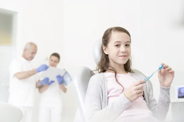 Retrato Menina Sorridente Segurando Escova Dentes Enquanto Sentado Contra Médicos — Fotografia de Stock