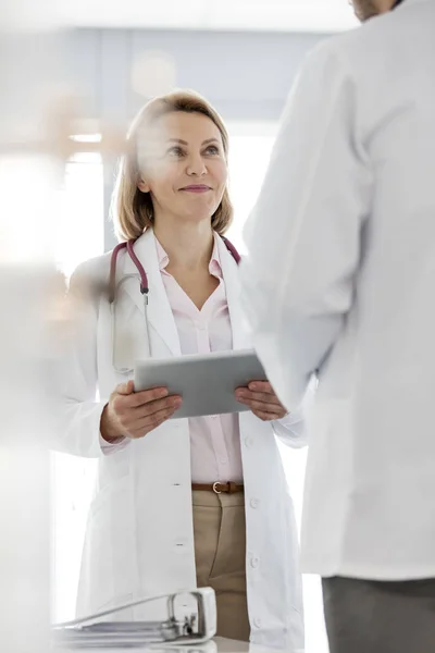 微笑的医生拿着数字平板电脑 在医院与同事讨论 — 图库照片