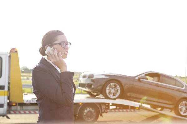 ビジネス プロフェッショナルのレッカー車が彼女の車をピックアップしながら電話で話しています — ストック写真