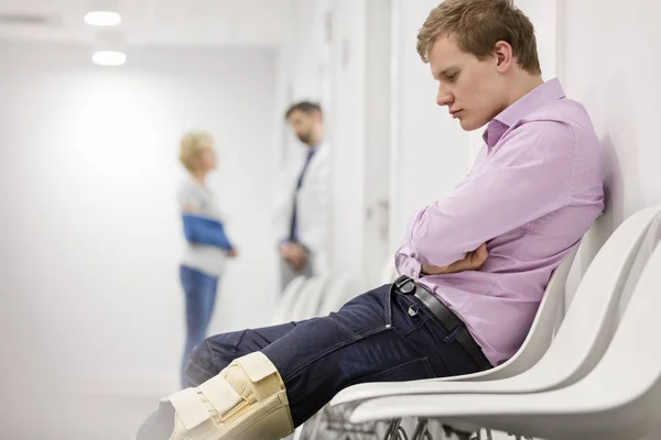 Homem Olhando Para Cinta Joelho Enquanto Sentado Sala Espera Hospital — Fotografia de Stock