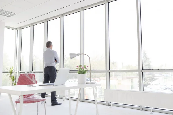 新しいオフィスで窓を通して見る思慮深い成熟したビジネスマンの完全な長さ — ストック写真